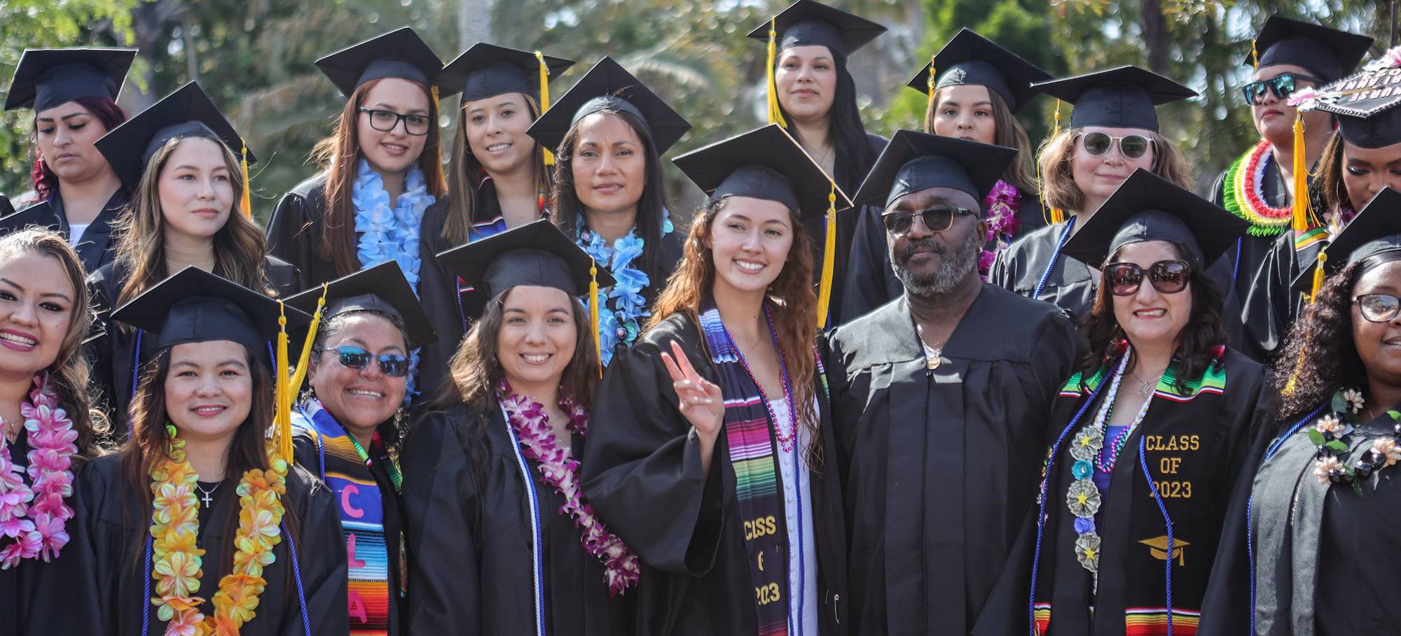 A group of students in black graduation caps and gowns. Some are wearing flower leis