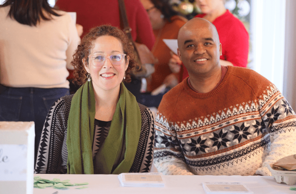 Two employees sitting at a welcome table at the holiday party