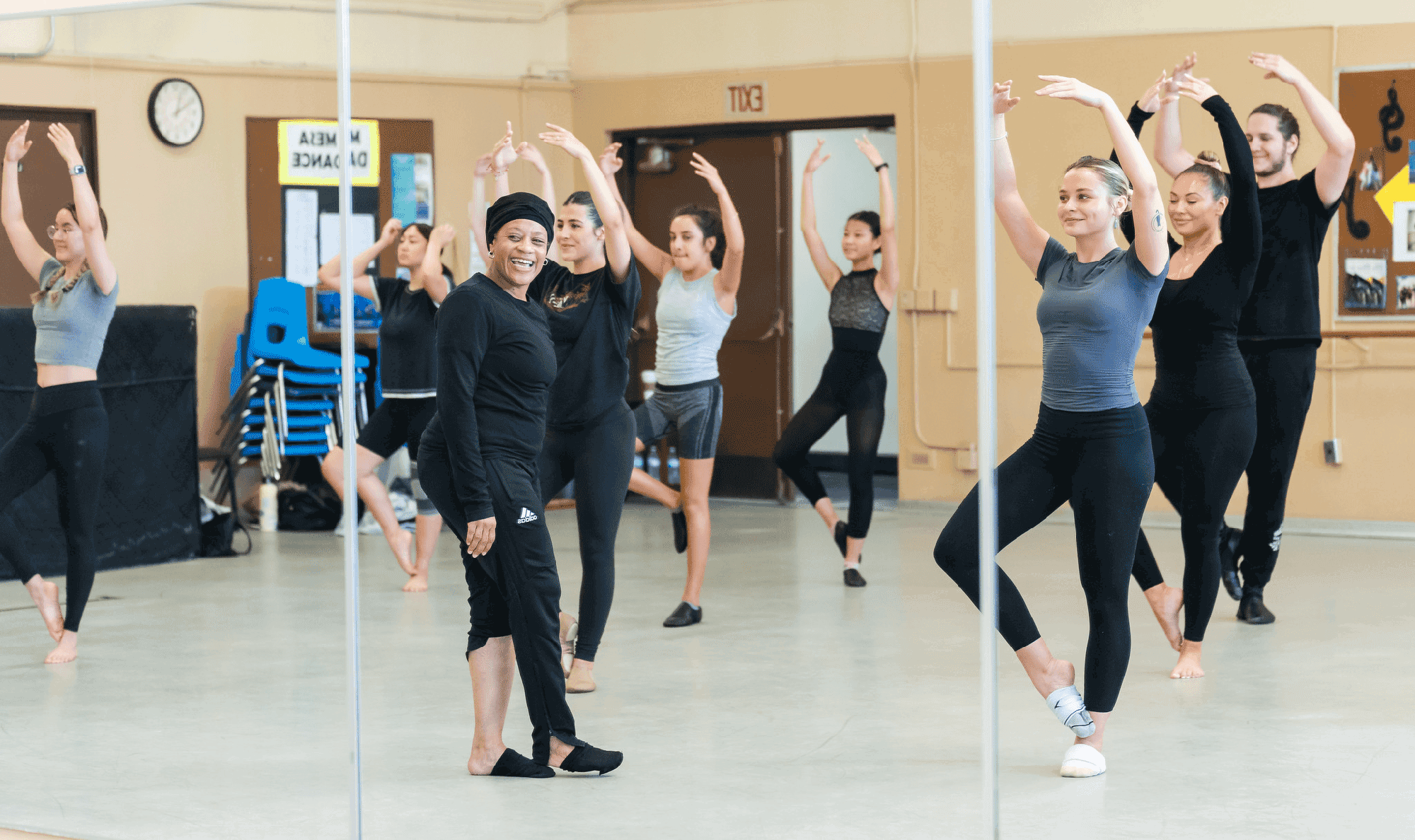 A dance instructor and her dance classes look in a mirror while dancing.
