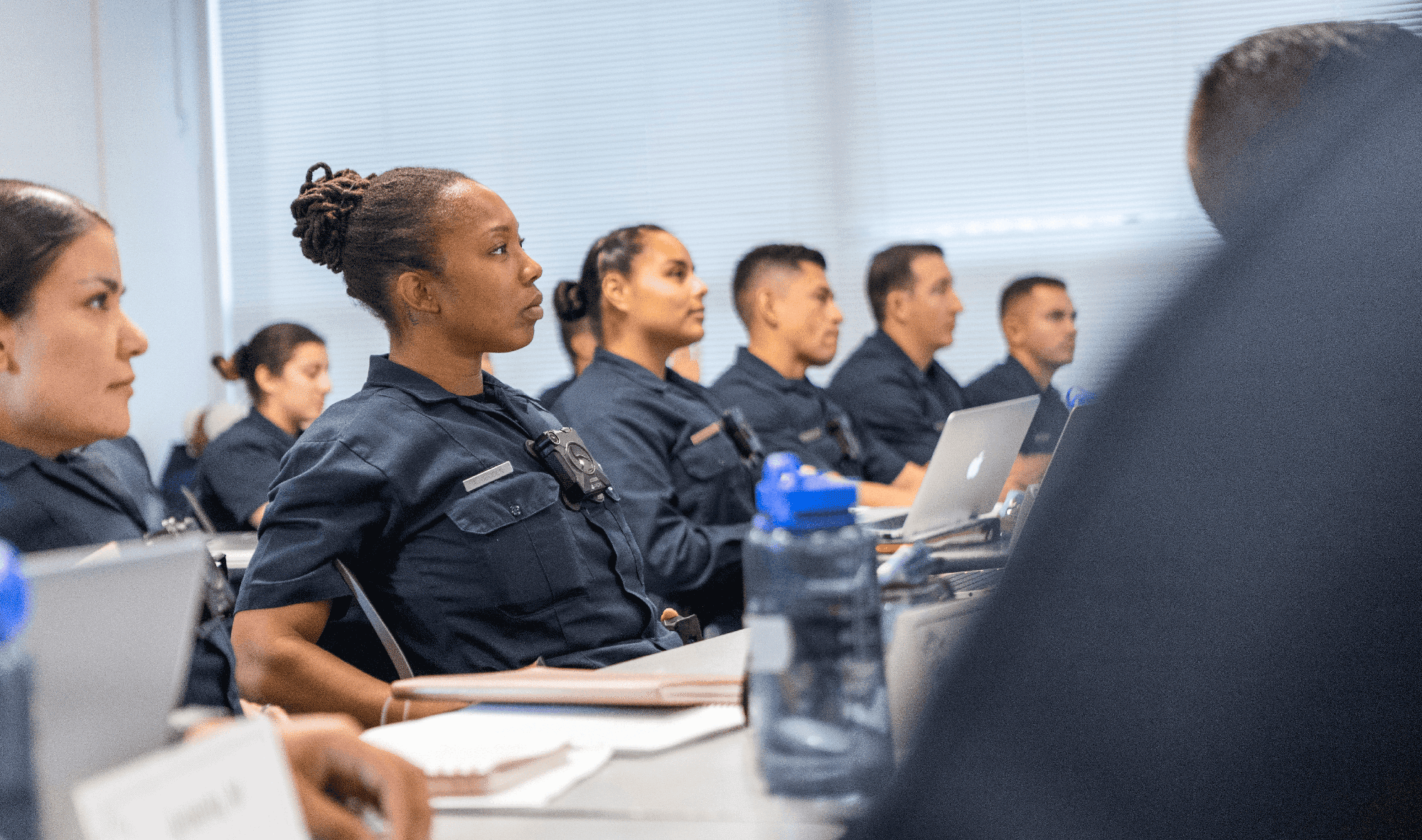 Students in police uniforms sit a tables in a classroom at the Miramar Police Academy