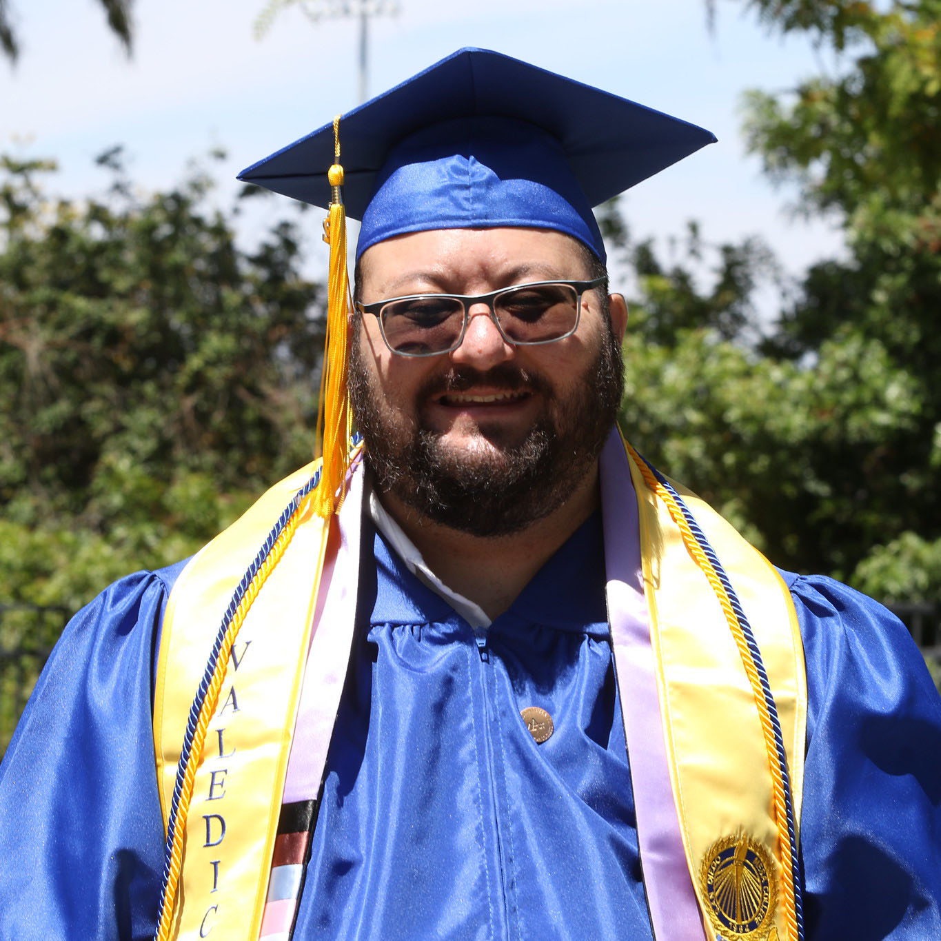 Danny Dunn is smiling and wearing glasses and blue and gold graduation attire.