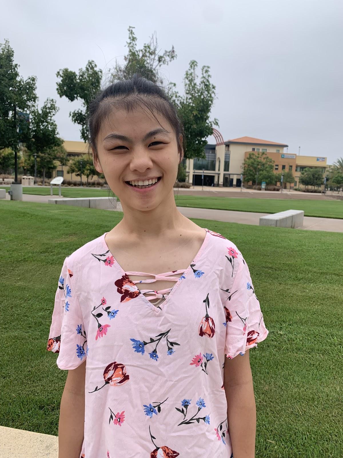 Yuhan stands on the Miramar campus wearing a pink floral shirt, smiling