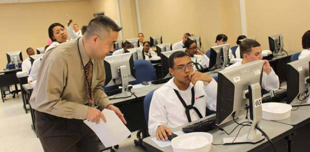 Sailors work at computer stations in a classroom
