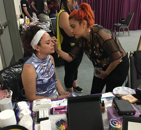 A student puts makeup on a person at comiccon