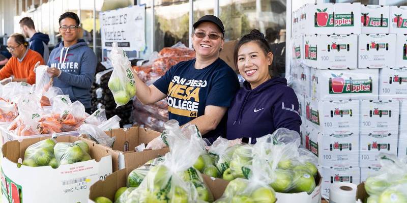 Two women at tables hand out fruit at the free farmers market