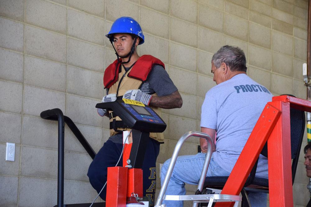 A firefighter in training climbs a stair machine while wearing 75 pounds as part of a training test