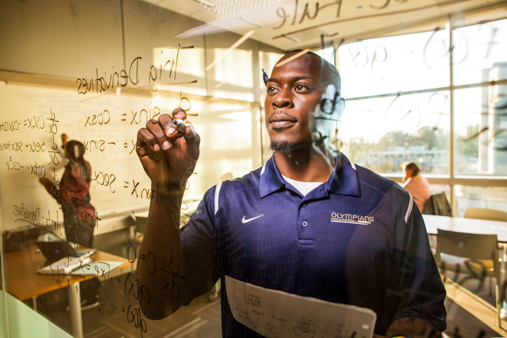 A Mesa College student works out a math equation on a glass wall.