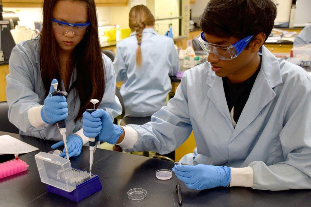 Two students use syringes to fill vials in a science lab.