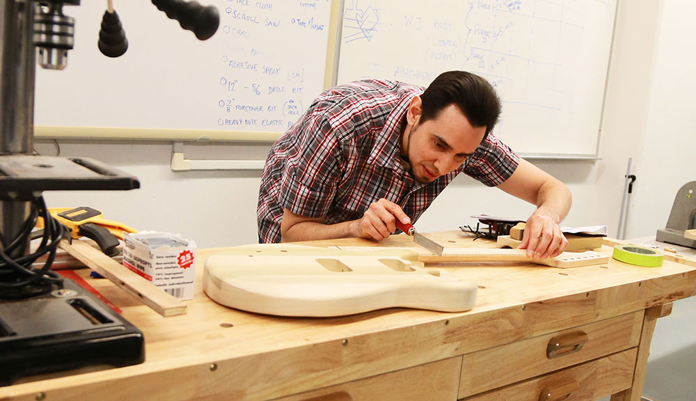 A City College student at a work bench shaping a guitar