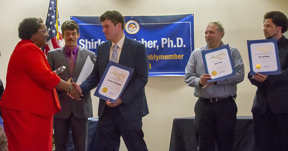 Carlos Turner Cortez shakes hands with Shirley Weber after receiving his award.