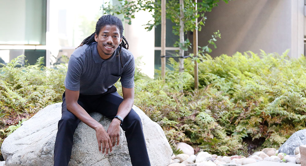 Henry Cunningham sits outside on a rock at Mesa College