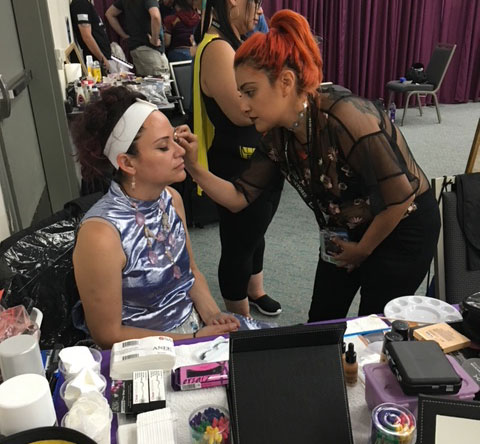 A student puts makeup on a person at comiccon