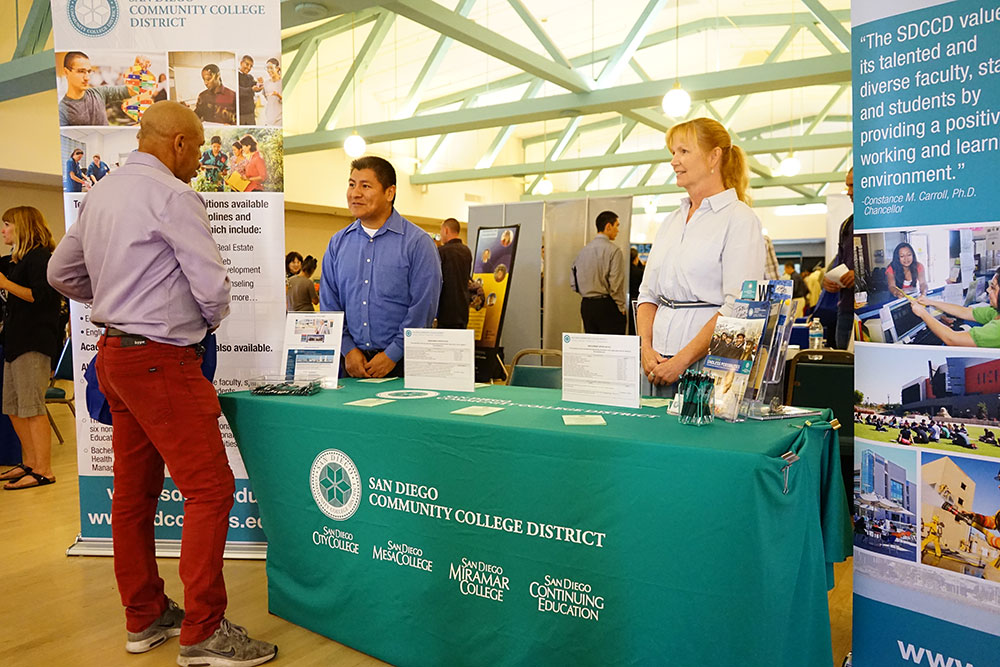 2 employees stand near a table set up at a previous job fair