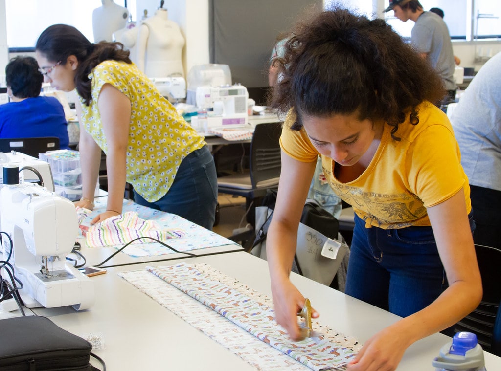 Two students cut fabric on a table.