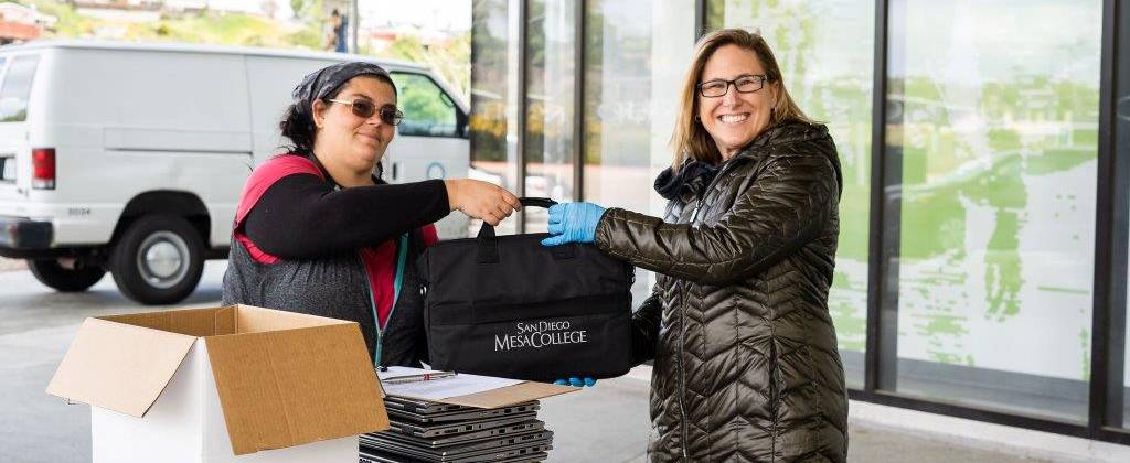 A staff member loans a laptop to a student