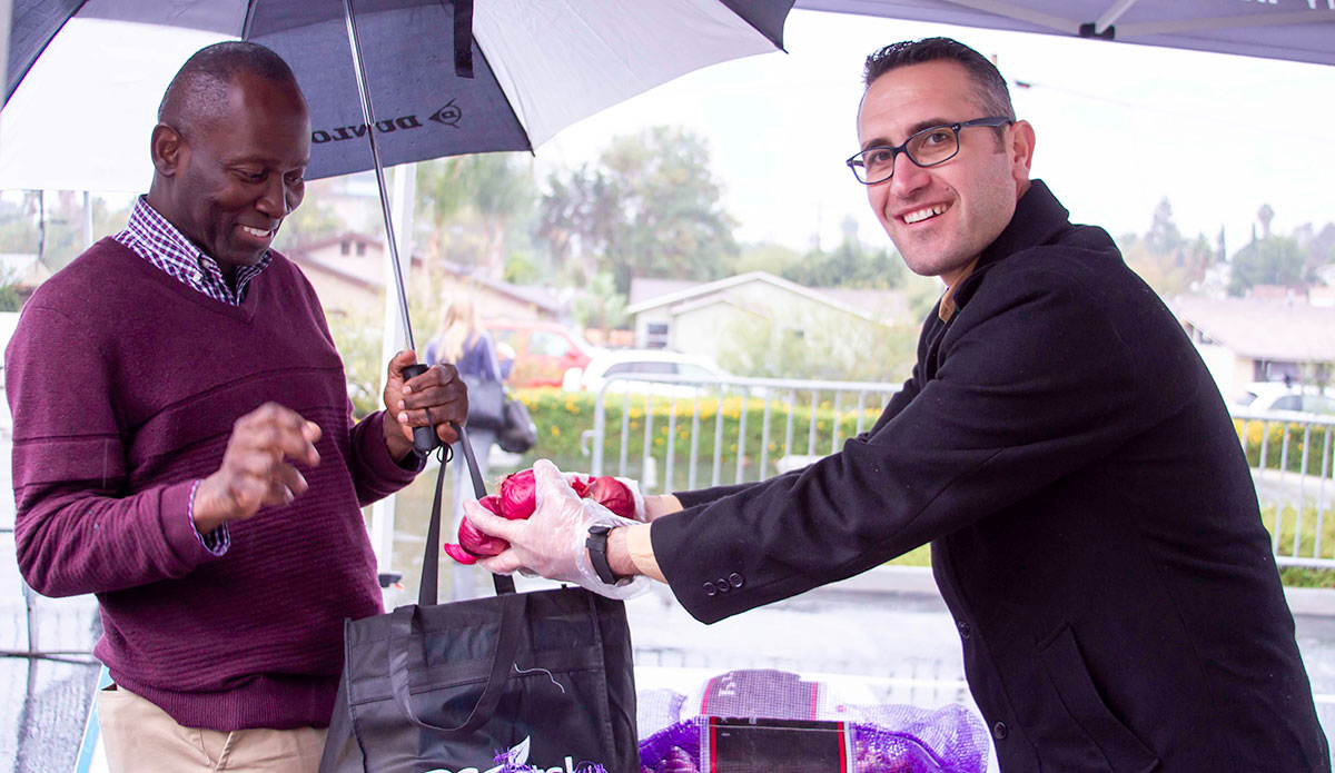 A volunteer hands over fresh red onions during SDCEats! at the Educational Cultural Complex.