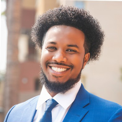 Dr. Abdimalik Buul is smiling and wearing a blue suit in a portrait photo