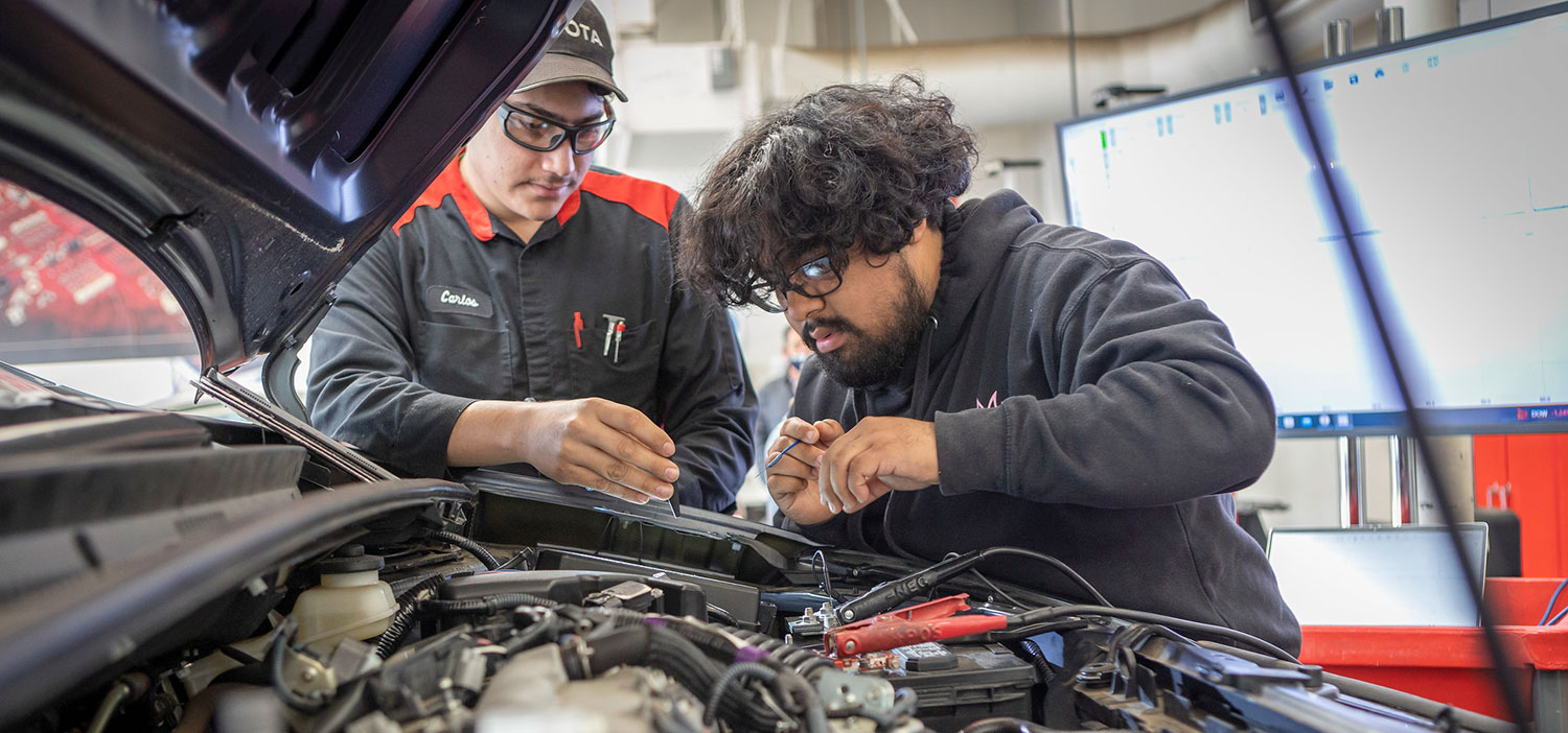 Autotech An autotech instructor and a student are wearing safety goggles and are working on a vehicle engine.