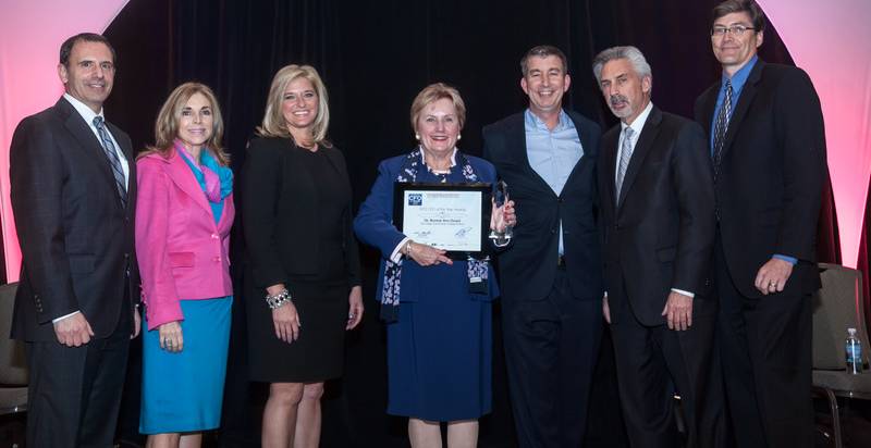 Bonnie Dowd on stage receiving her award. Six others are with her and posing together for a photograph