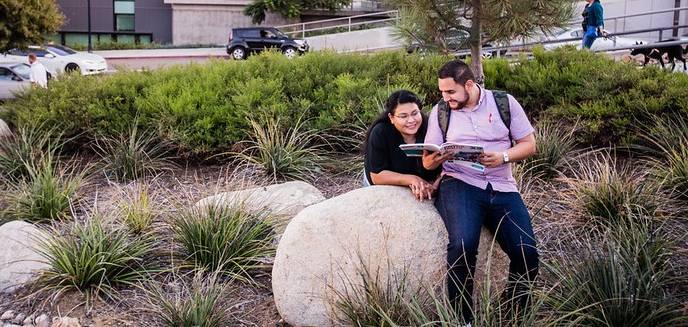 Two students look at a book in a garden outside of City College