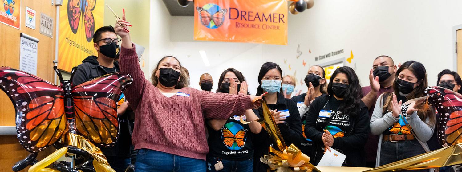 A group of students and staff cheer as a golden ribbon is cut to celebrate the grand opening of the dreamer center at Mesa College