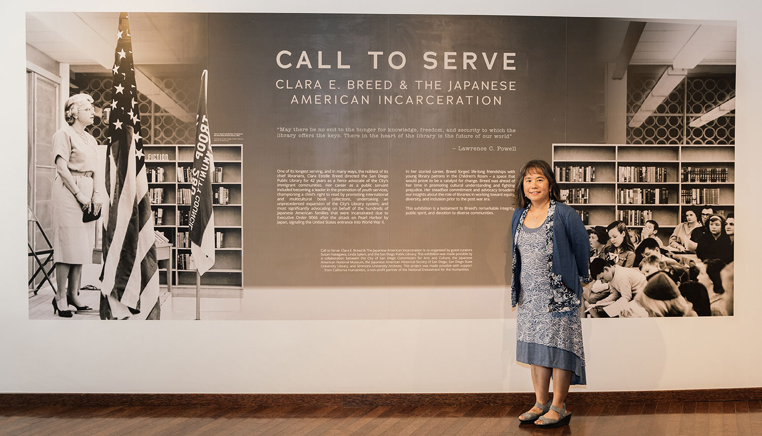 Susan Hasegawa stands in front of a mural that describes the incarceration of Japanese Americans during World War Two