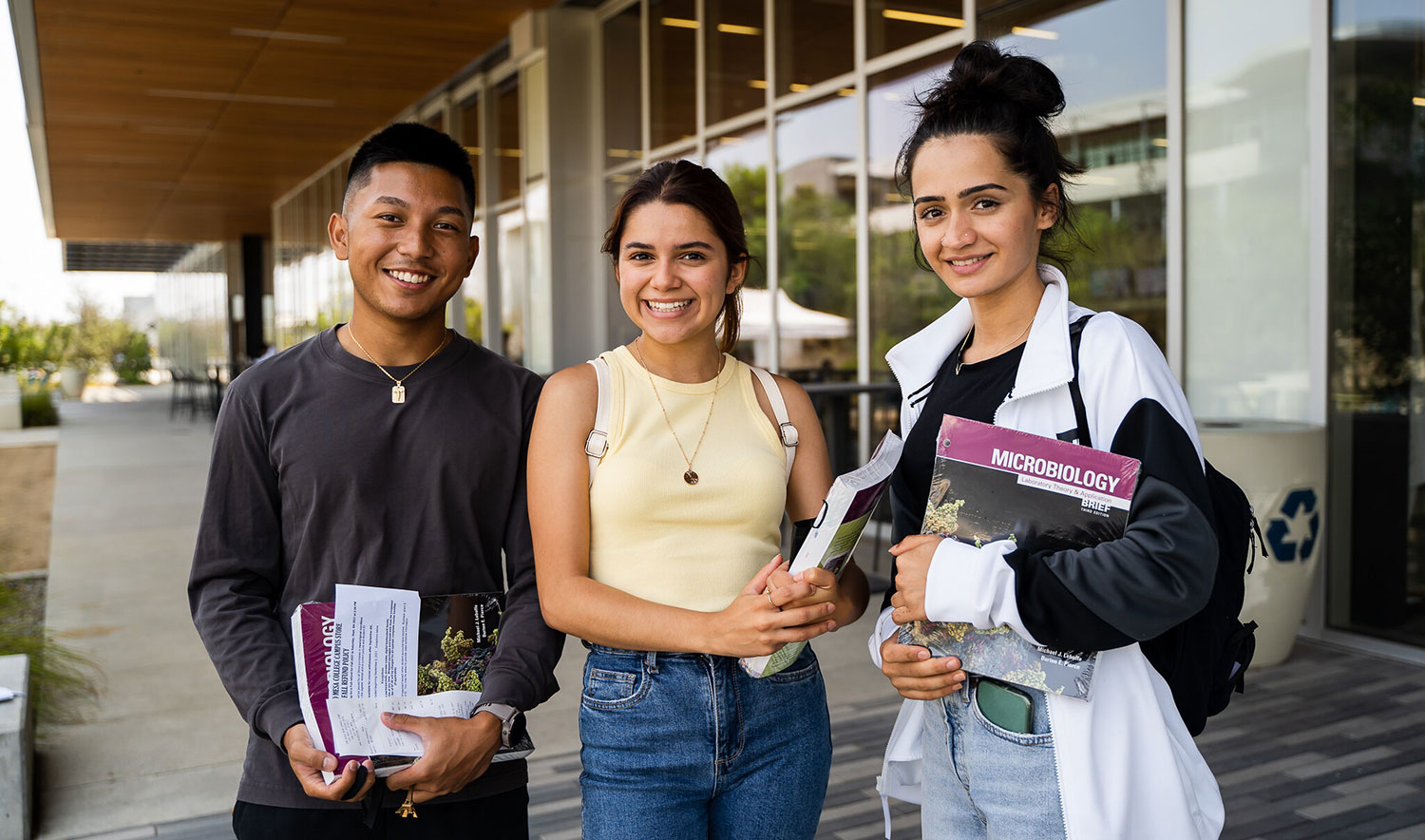 Three students hold their books in front of the Mesa Commons building