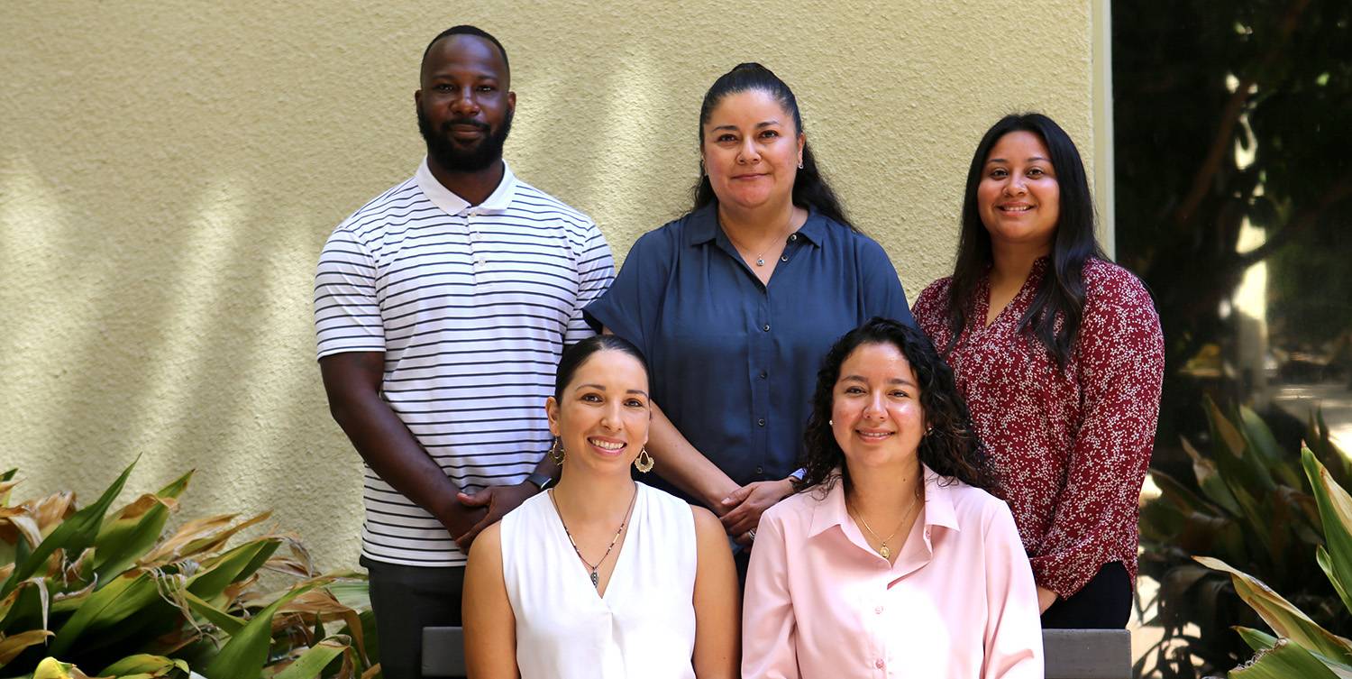 Two outreach coordinators sit on a bench and three are standing behind them for a group photo.