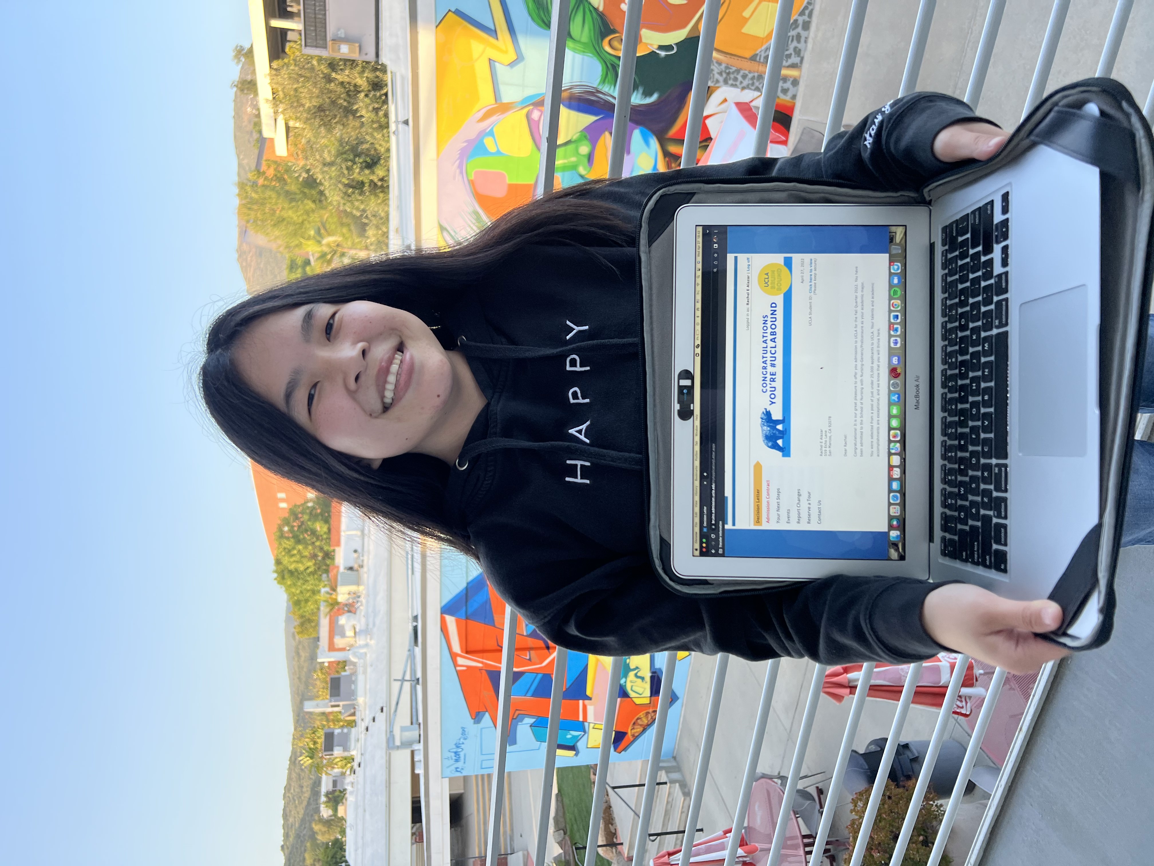 Rachel Alazar wears a black sweatshirt and holds out her laptop computer