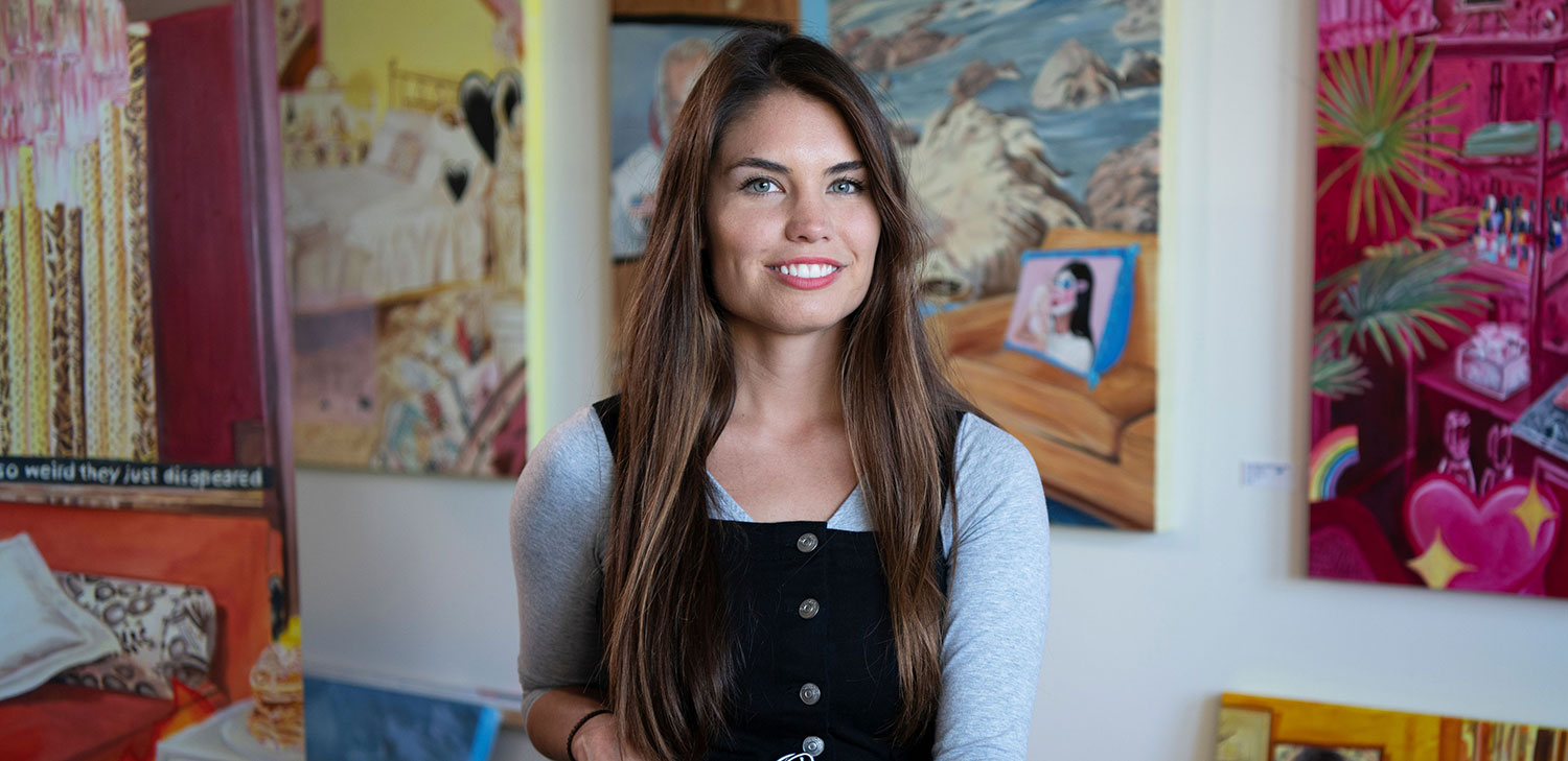 Faculty member Remi Dalton with colorful artwork behind her