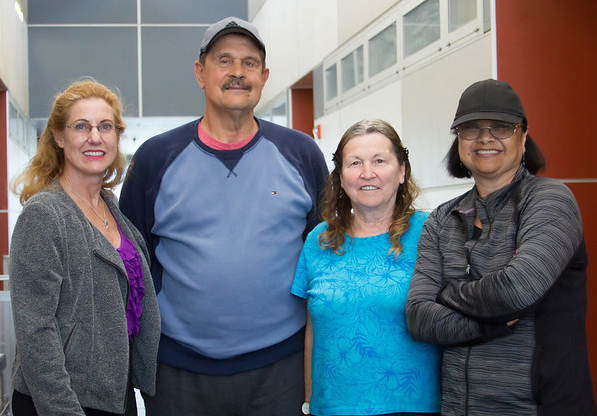 Four people take a group photo in a hallway of a campus building