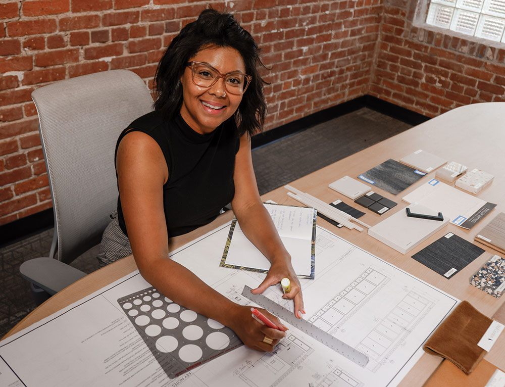 Bianca McLaughlin sits at her desk with design drawings and drawing tools