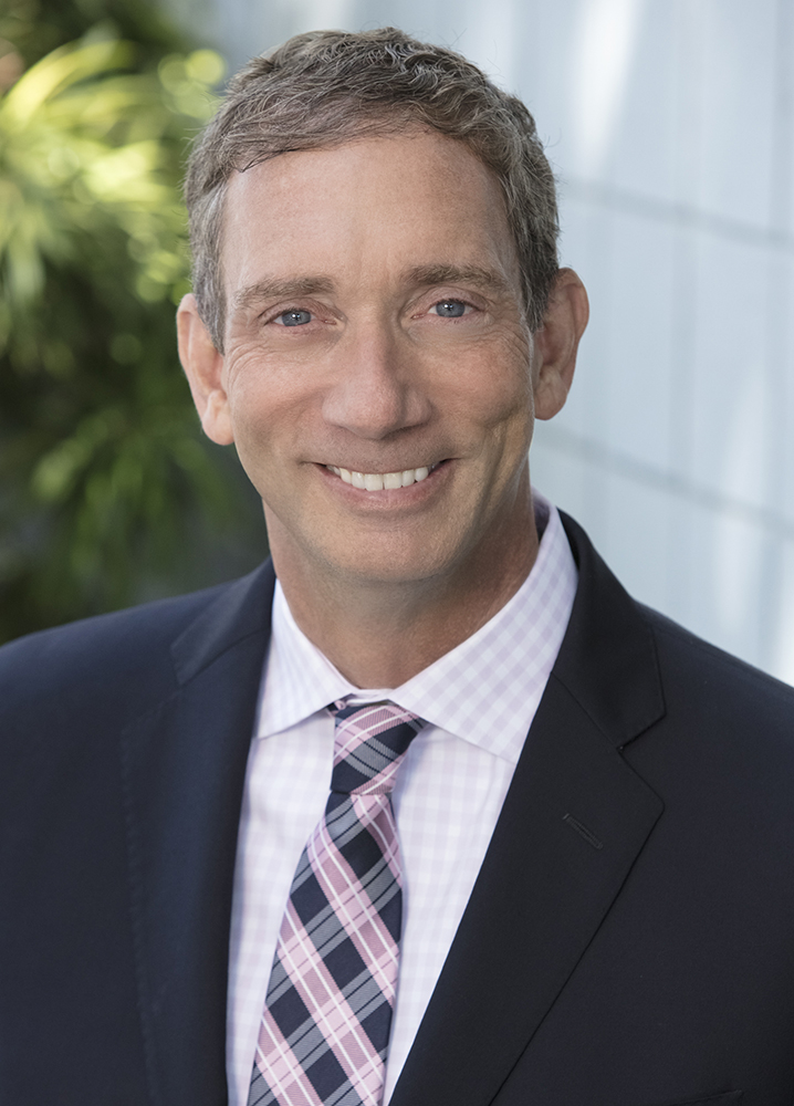 Portrait photo of Brian King wearing a black suit a white shirt and a pink and black tie