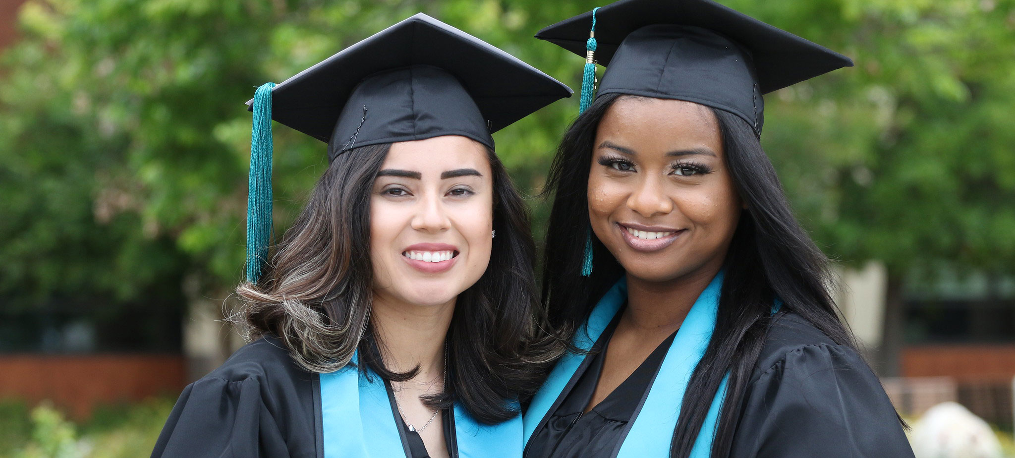 Two graduates in black caps and gowns with a teal Miramar sash