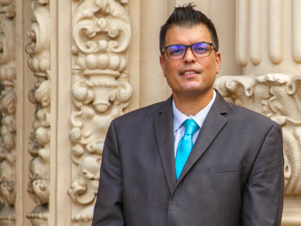 Dr. Carlos Cortez wears a gray suit and a bright teal tie