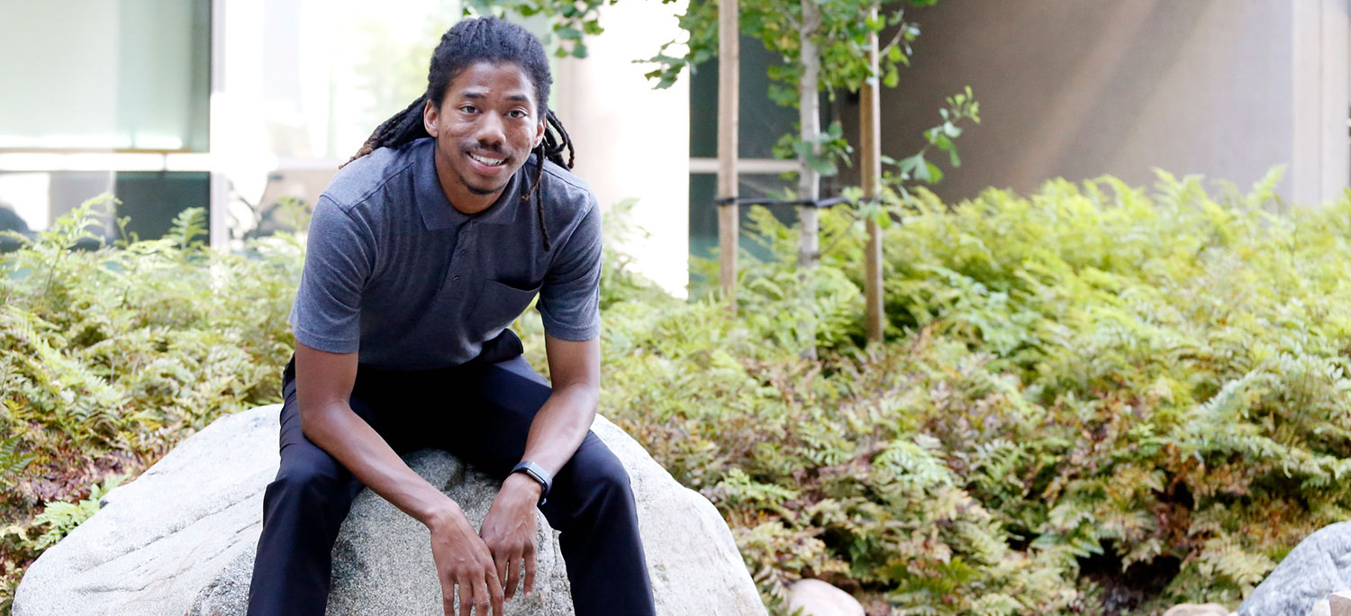 Henry Cunningham sits on a large rock in a garden at Mesa College