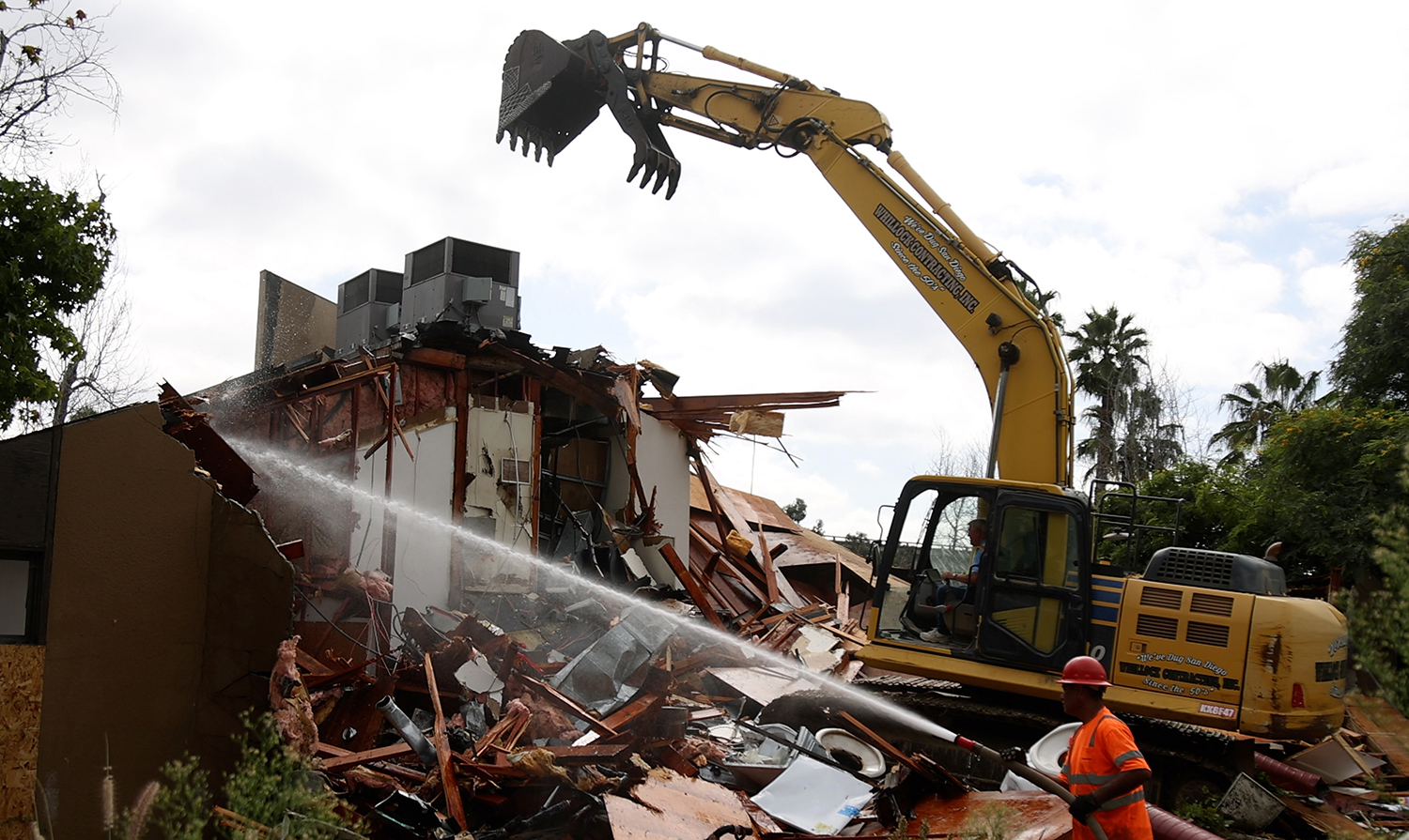 A demolition crew with an earth mover tears down a old building.