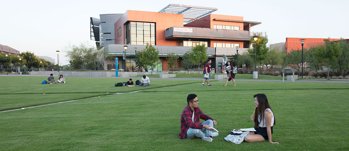 Two students sit on the lawn at compass point on Miramar College's campus. The student services building is in the background