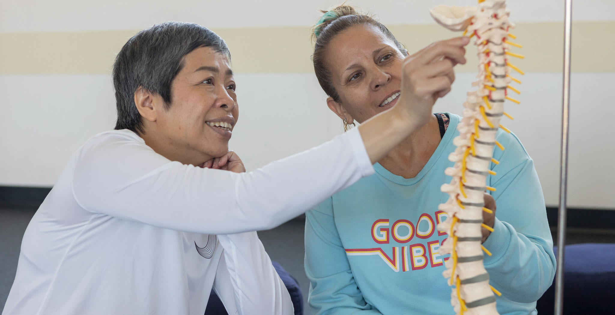 A yoga instructor shows a student a skeletal display of a spine