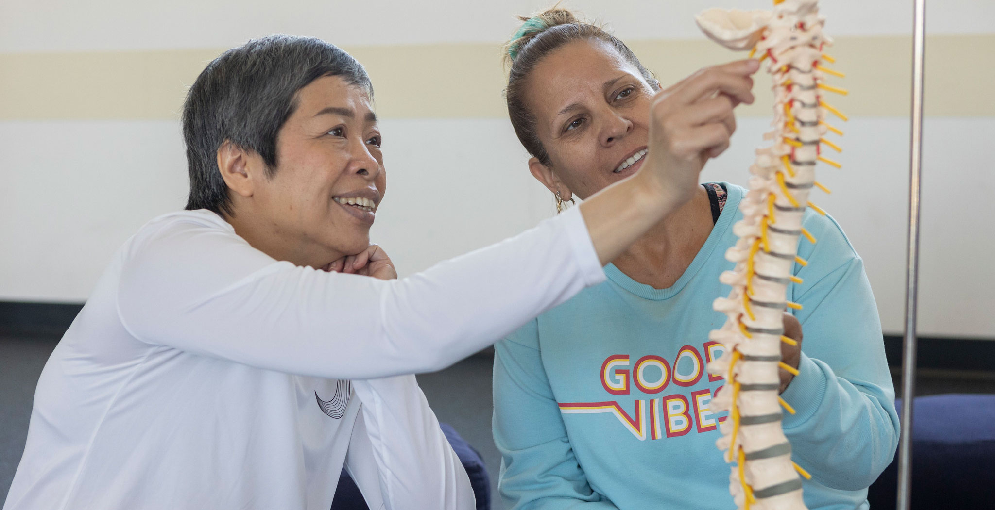 A yoga instructor shows a student a skeletal display of a spine 