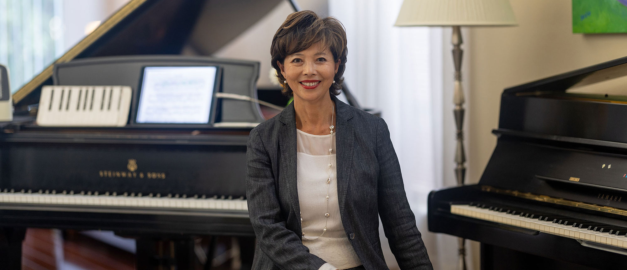 Helena Wei sits on a bench next to two pianos
