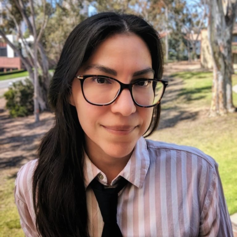 andrea zelaya wearing black glasses and a light pink striped collared shirt with a black tie