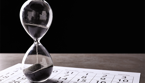 An hourglass on top of a paper calendar