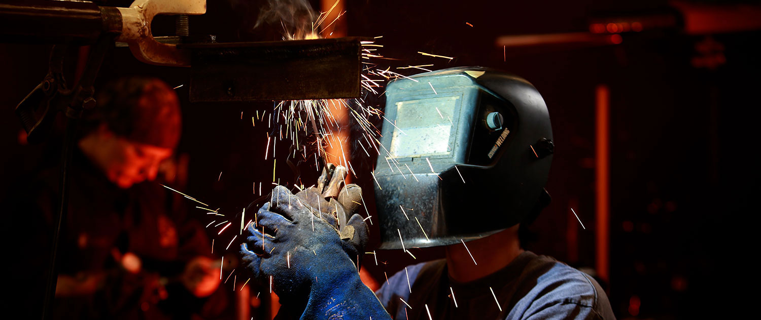 A welding student is wearing a welding mask and using a torch