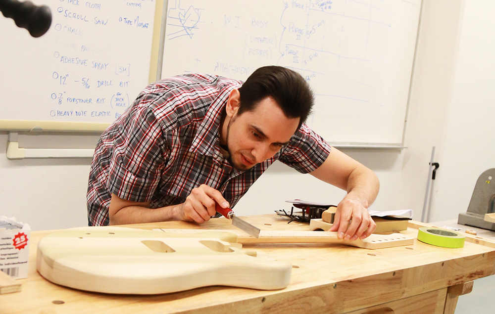 A City College student at a work bench shaping a guitar