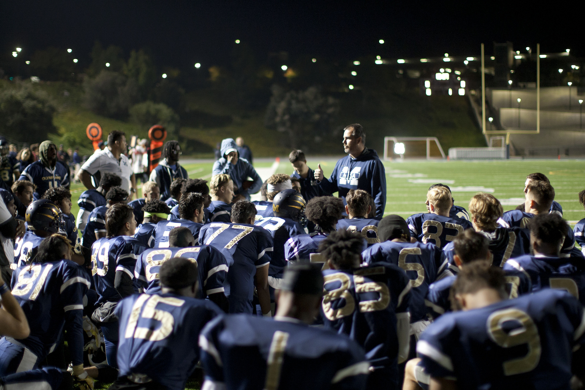 Mesa College football coach talks to the team on the field during a night game