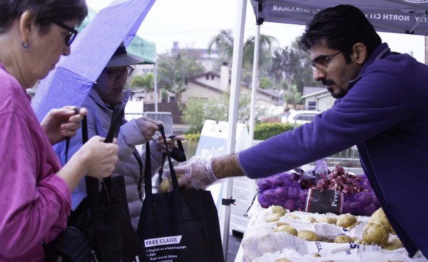 An employee puts produce into two ladies canvas bads at the free farmers market