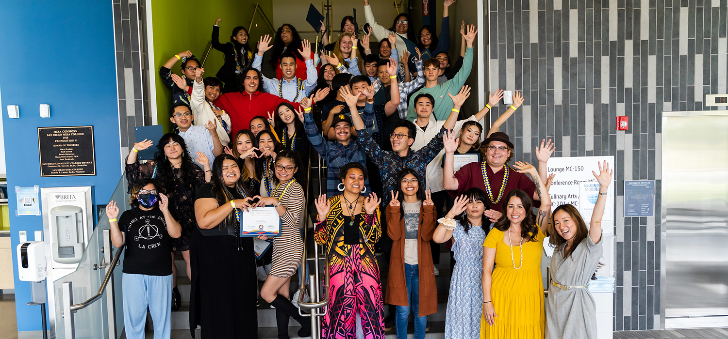 A group of about 50 people gather on the stairs for a group photo. They have their hands in the air cheering.
