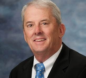 A portrait photo of Bernie Rhinerson. He is wearing a black jacket, white shirt and a bright blue tie
