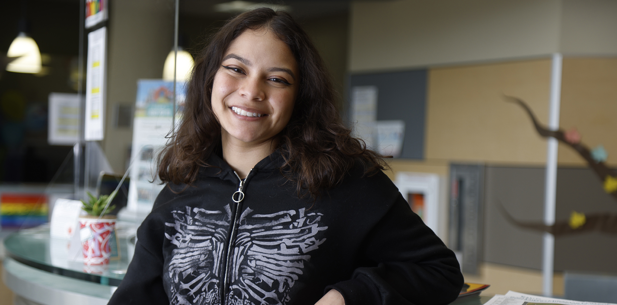 Breanna Hinojosa wearing a black sweatshirt leans on the counter at the outreach office at Miramar College